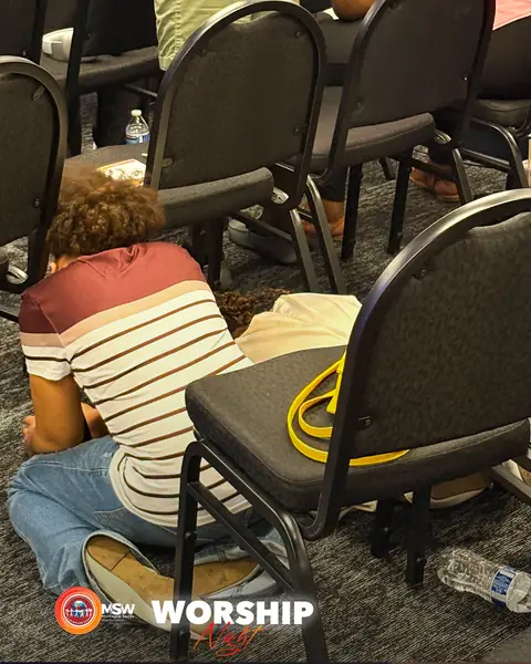 A member kneeling on the floor beside a chair in prayer